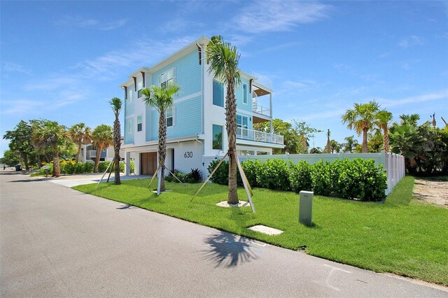 exterior space featuring driveway, a balcony, an attached garage, fence, and a yard