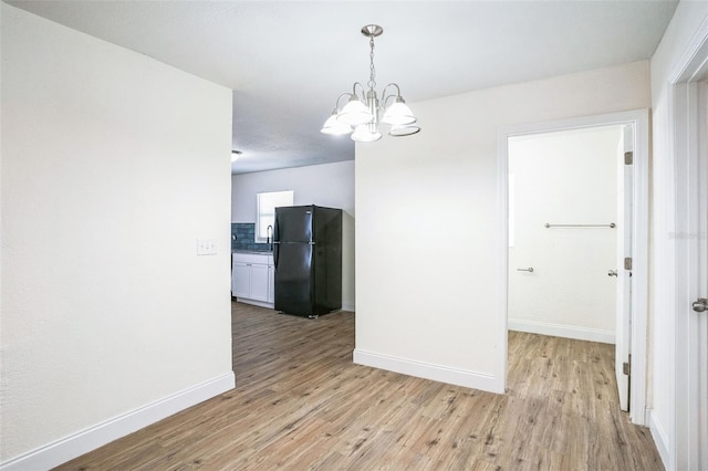 unfurnished dining area featuring sink, light hardwood / wood-style floors, and a notable chandelier