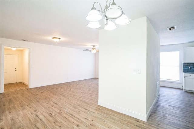 empty room with ceiling fan with notable chandelier, light hardwood / wood-style floors, and a textured ceiling