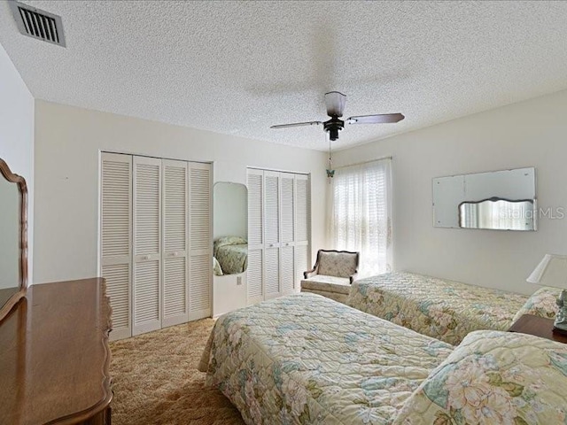 carpeted bedroom with a textured ceiling, ceiling fan, and two closets