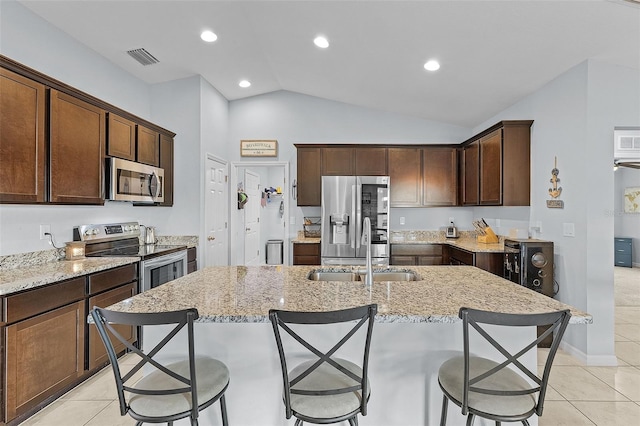 kitchen with lofted ceiling, stainless steel appliances, a center island with sink, and light tile patterned floors