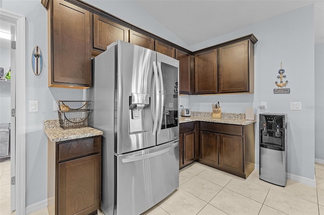 kitchen with stainless steel fridge, light stone counters, lofted ceiling, and light tile patterned floors