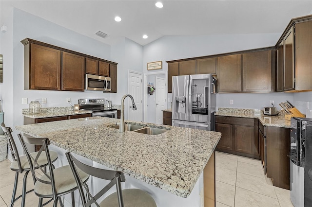 kitchen featuring sink, lofted ceiling, light stone countertops, a kitchen island with sink, and appliances with stainless steel finishes