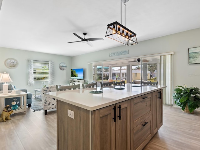 kitchen with ceiling fan with notable chandelier, a kitchen island, light hardwood / wood-style floors, and decorative light fixtures