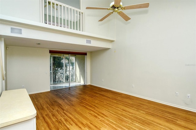 unfurnished living room with ceiling fan, hardwood / wood-style floors, and a towering ceiling