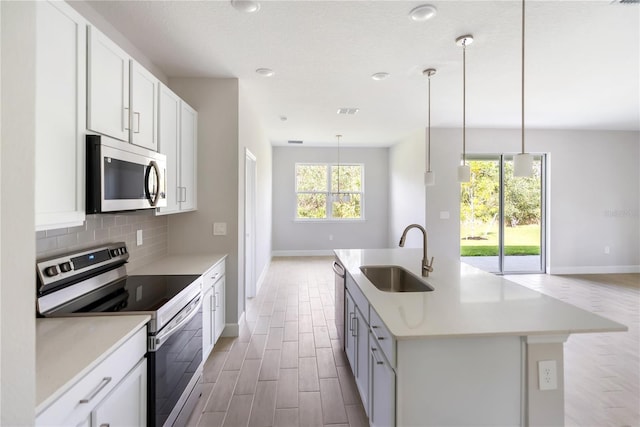 kitchen with stainless steel appliances, sink, pendant lighting, white cabinetry, and an island with sink