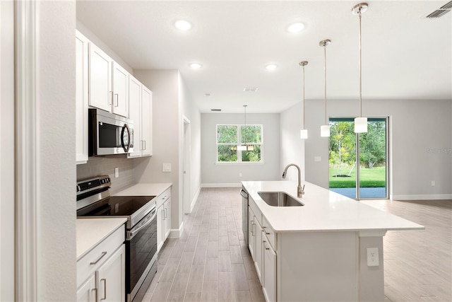 kitchen featuring backsplash, white cabinets, sink, appliances with stainless steel finishes, and decorative light fixtures