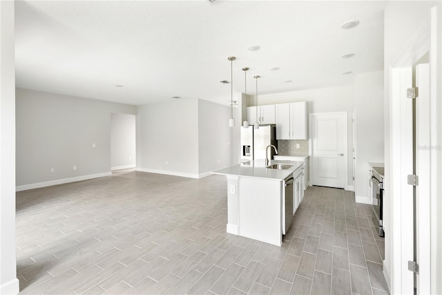 kitchen with hanging light fixtures, stainless steel appliances, tasteful backsplash, a kitchen island with sink, and white cabinets