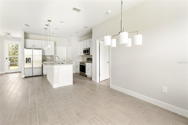 kitchen with decorative light fixtures, decorative backsplash, a center island with sink, white cabinets, and appliances with stainless steel finishes