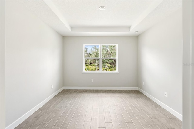 empty room featuring a tray ceiling, light hardwood / wood-style flooring, and a textured ceiling