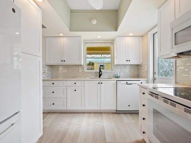 kitchen with decorative backsplash, light wood-type flooring, white appliances, sink, and white cabinetry