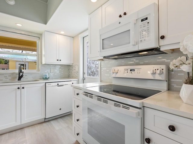 kitchen featuring white appliances, white cabinets, sink, light hardwood / wood-style flooring, and decorative backsplash