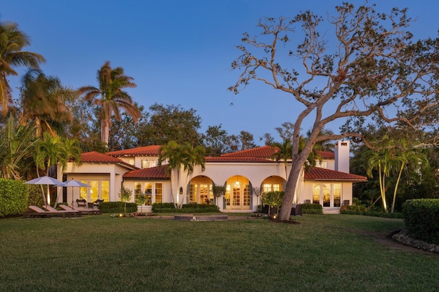 back of house with stucco siding, a tiled roof, french doors, and a yard
