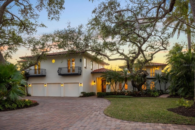 mediterranean / spanish home featuring stucco siding, an attached garage, a tiled roof, a balcony, and decorative driveway