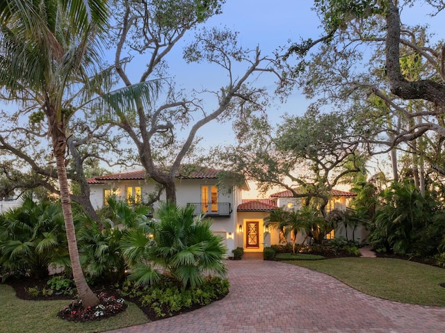 mediterranean / spanish-style house with a balcony, decorative driveway, a tile roof, a front lawn, and stucco siding