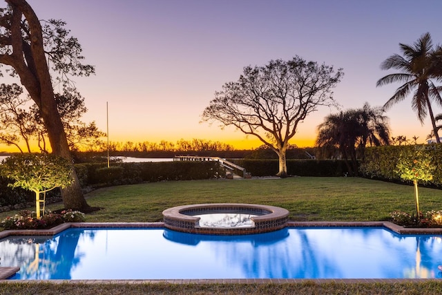 pool at dusk with a lawn and a pool with connected hot tub