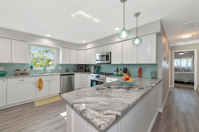 kitchen with pendant lighting, appliances with stainless steel finishes, light stone counters, white cabinets, and kitchen peninsula