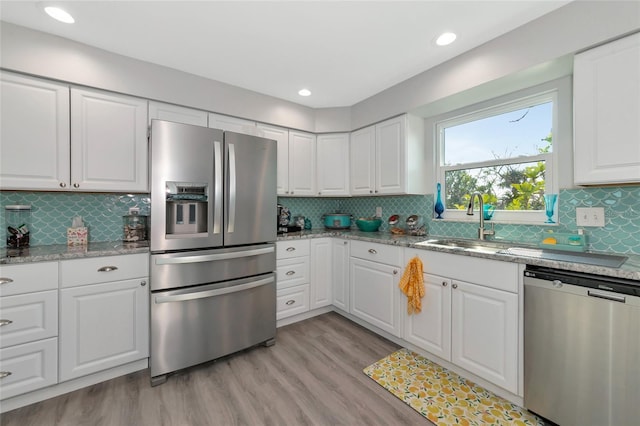 kitchen with sink, light stone counters, light hardwood / wood-style flooring, appliances with stainless steel finishes, and white cabinets