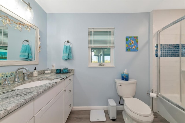 full bathroom featuring vanity, wood-type flooring, bath / shower combo with glass door, and toilet