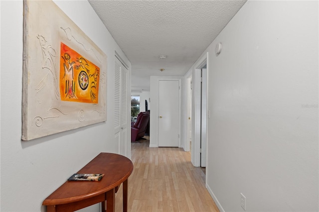 hall featuring light wood-type flooring and a textured ceiling