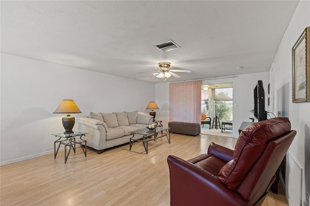 living room with ceiling fan, a textured ceiling, and light wood-type flooring