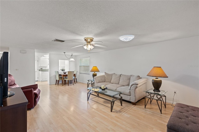 living room featuring ceiling fan, a textured ceiling, and light wood-type flooring