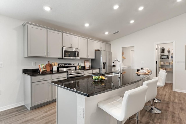 kitchen with a kitchen bar, a center island with sink, appliances with stainless steel finishes, gray cabinetry, and sink