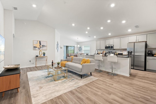 living room featuring light hardwood / wood-style floors, a chandelier, and vaulted ceiling