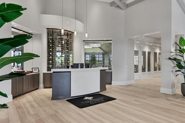 bar featuring decorative light fixtures, beam ceiling, light wood-type flooring, and a high ceiling