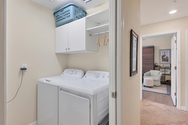 clothes washing area featuring separate washer and dryer, light tile patterned floors, and cabinets