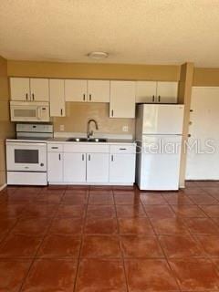 kitchen featuring white cabinetry, sink, dark tile patterned flooring, and white appliances