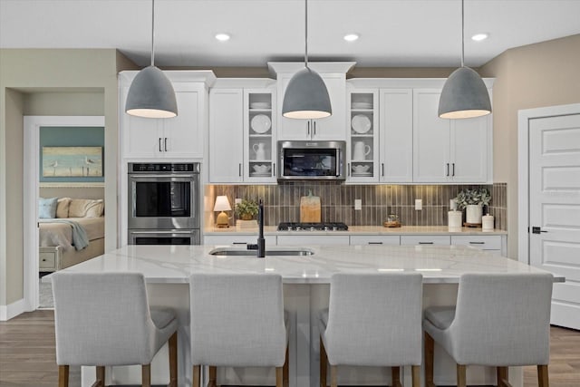 kitchen with decorative backsplash, appliances with stainless steel finishes, a kitchen island with sink, sink, and hanging light fixtures