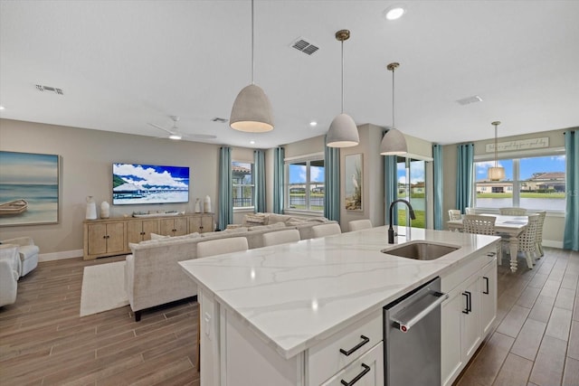 kitchen with an island with sink, sink, white cabinets, and pendant lighting