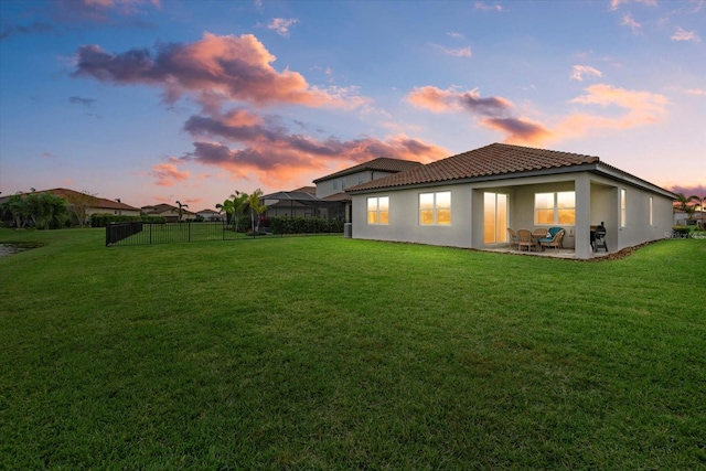 back house at dusk with a lawn and a patio