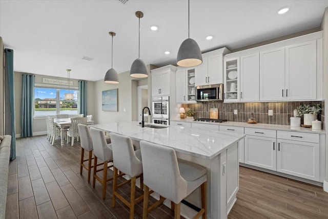 kitchen featuring a center island with sink, white cabinets, sink, appliances with stainless steel finishes, and decorative light fixtures