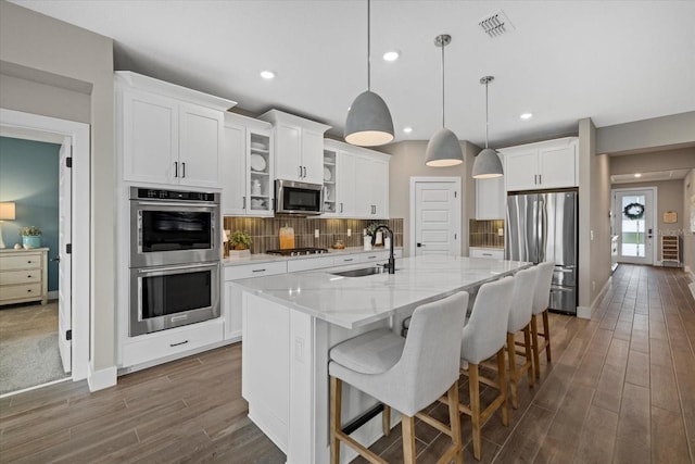 kitchen featuring a kitchen island with sink, hanging light fixtures, sink, white cabinetry, and stainless steel appliances