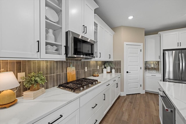 kitchen with stainless steel appliances, tasteful backsplash, light stone counters, white cabinets, and light wood-type flooring