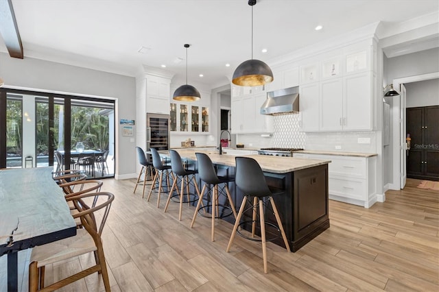 kitchen featuring white cabinetry, hanging light fixtures, range hood, an island with sink, and a kitchen bar