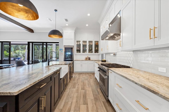 kitchen with ventilation hood, high end stainless steel range oven, decorative light fixtures, a center island with sink, and white cabinets