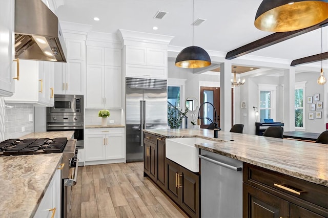 kitchen with beam ceiling, wall chimney range hood, built in appliances, decorative backsplash, and white cabinets