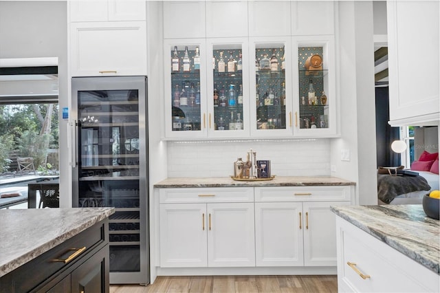 kitchen featuring white cabinets, light stone countertops, backsplash, and beverage cooler