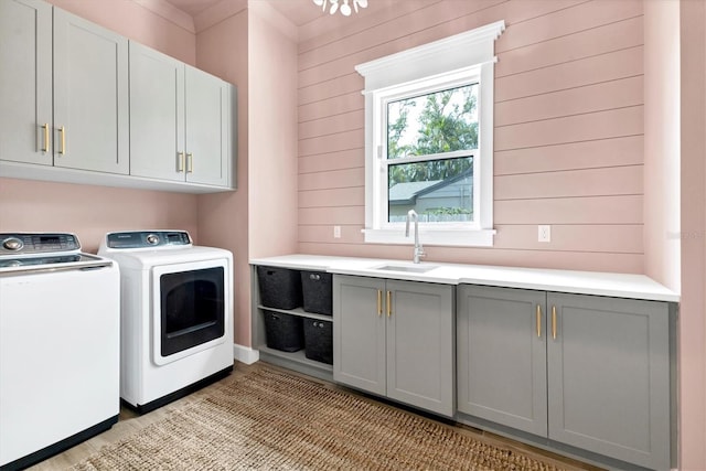 washroom with cabinets, independent washer and dryer, wooden walls, and sink