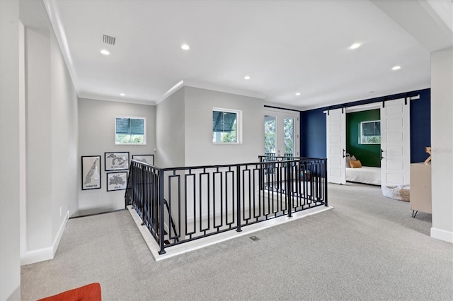 hall with a barn door, light colored carpet, and crown molding