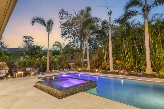 pool at dusk featuring an outdoor hangout area, an in ground hot tub, and a patio