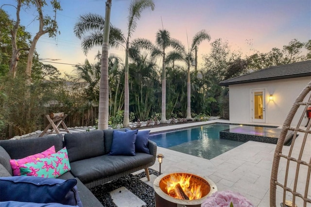 pool at dusk featuring an in ground hot tub, an outdoor living space with a fire pit, and a patio area