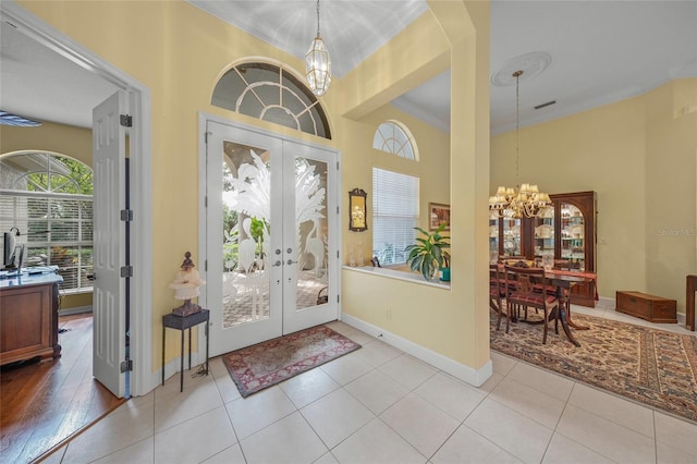 foyer with french doors, light tile patterned floors, ornamental molding, and a notable chandelier