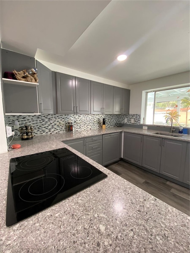 kitchen with gray cabinets, dark hardwood / wood-style floors, black stovetop, tasteful backsplash, and sink