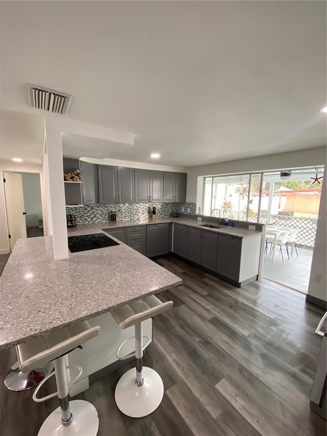 kitchen with a kitchen bar, light stone counters, tasteful backsplash, dark hardwood / wood-style floors, and gray cabinets