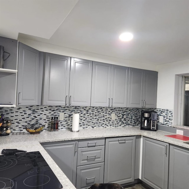 kitchen featuring black cooktop, light stone countertops, decorative backsplash, and gray cabinetry