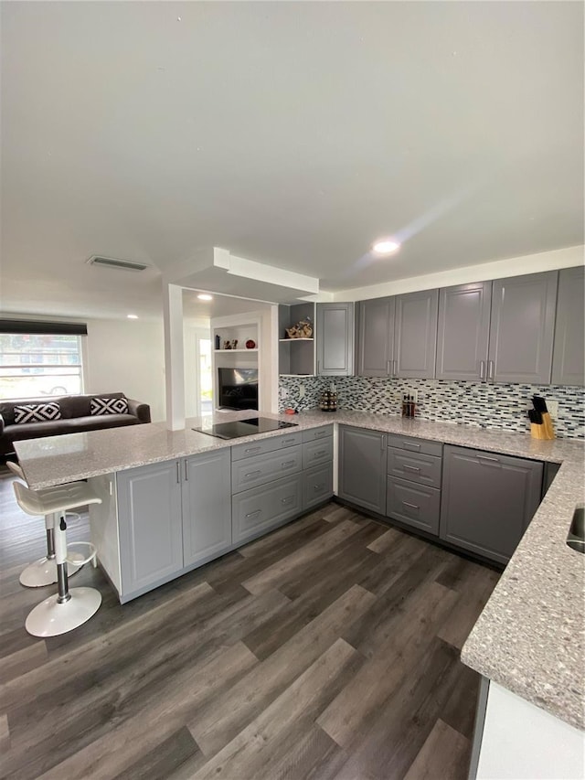 kitchen featuring gray cabinets, a breakfast bar, tasteful backsplash, light stone countertops, and dark wood-type flooring